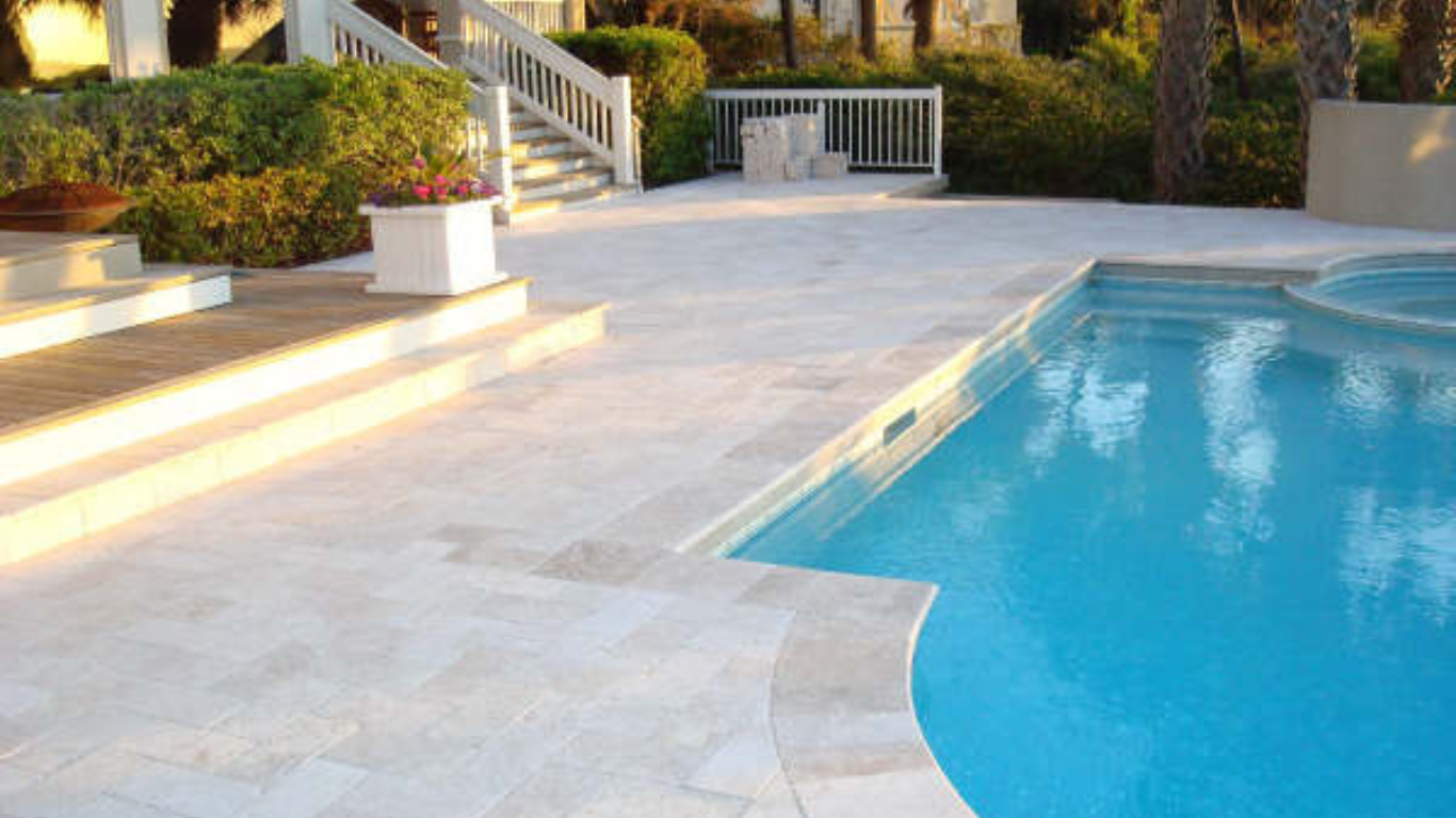 A person power-washing a sunlit patio made of Travertine Pavers, highlighting their smooth texture, durability, and appeal for outdoor spaces.